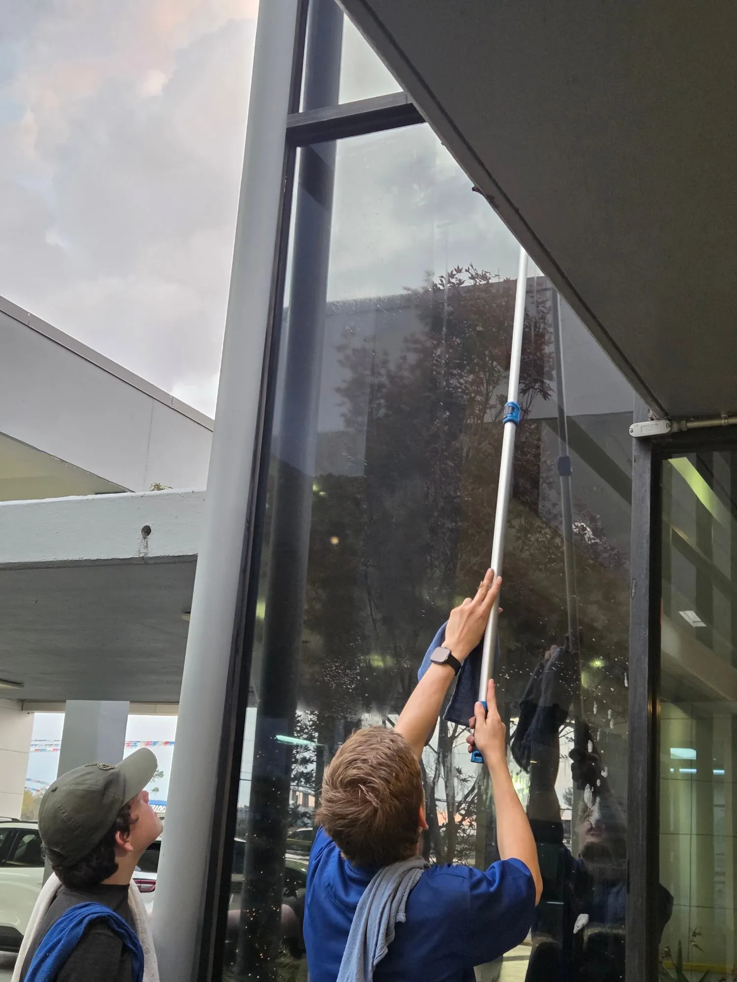 Two young window cleaners work a pole up a tall pane of commercial glass